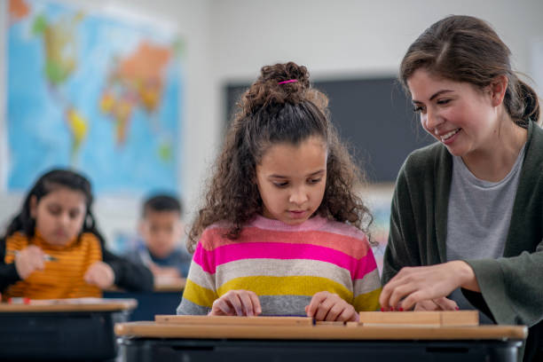 A teacher helping a young girl with hands-on learning at her desk in a Montessori classroom
