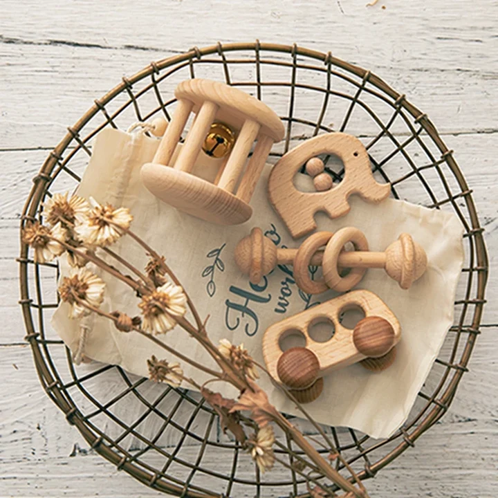 Wooden Montessori baby rattles and teethers in a wire basket with dried flowers on a white wood background