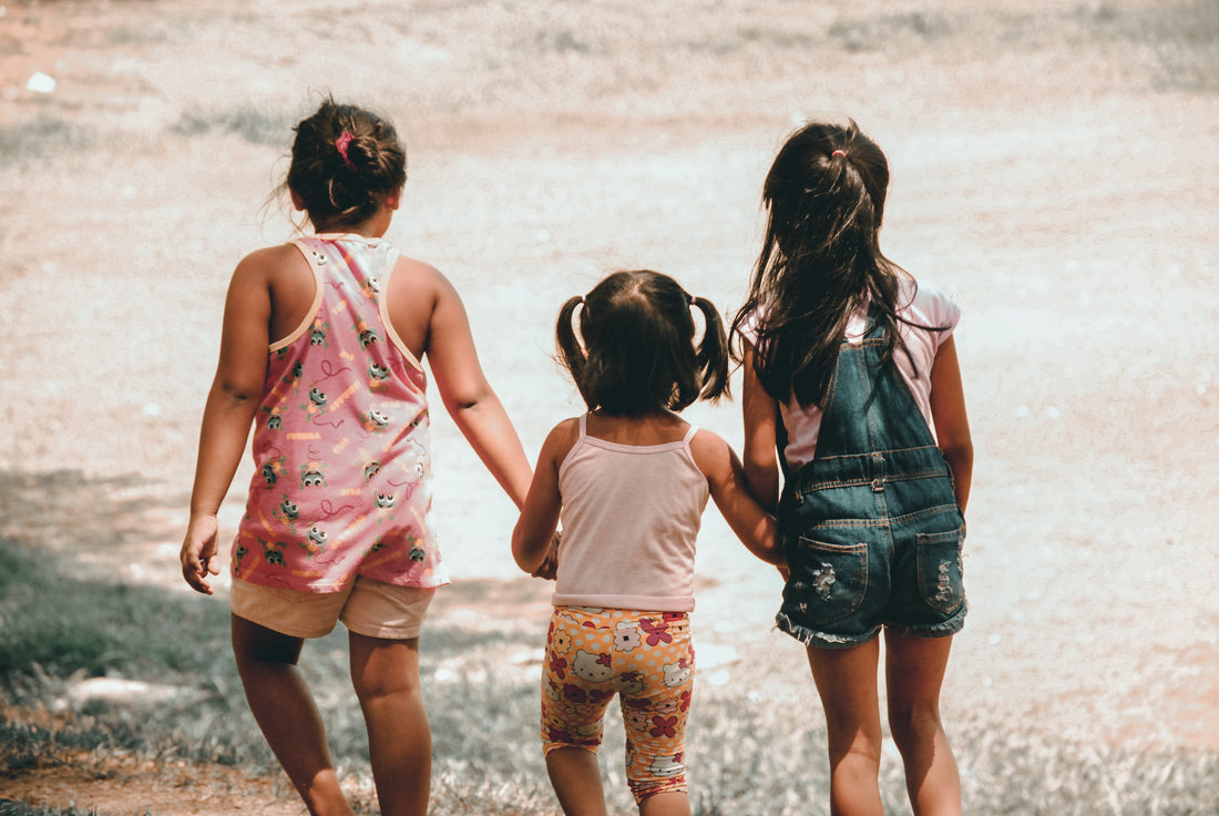 three children holding hands walking in the outdoors