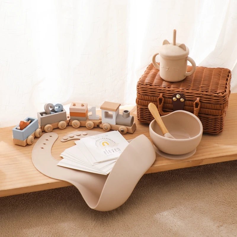 Wooden table with Montessori toys, a wicker basket, a ceramic bowl with a spoon, and a stack of white paper.