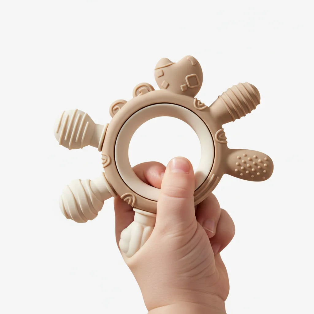 A beige silicone baby teether with textured sensory bumps and a cat-shaped handle, held in a baby's hand against a clean white background.