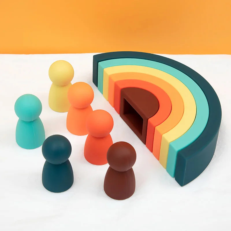 Colorful silicone toys including a rainbow-shaped block and small figurines on a white surface with an orange background.