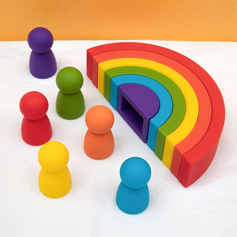 Colorful silicone rainbow toy and peg people on a white surface with an orange background