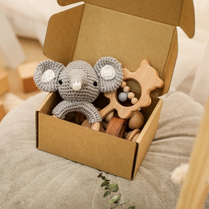 Box with a gray crocheted mouse toy and wooden star rattle on a soft surface.