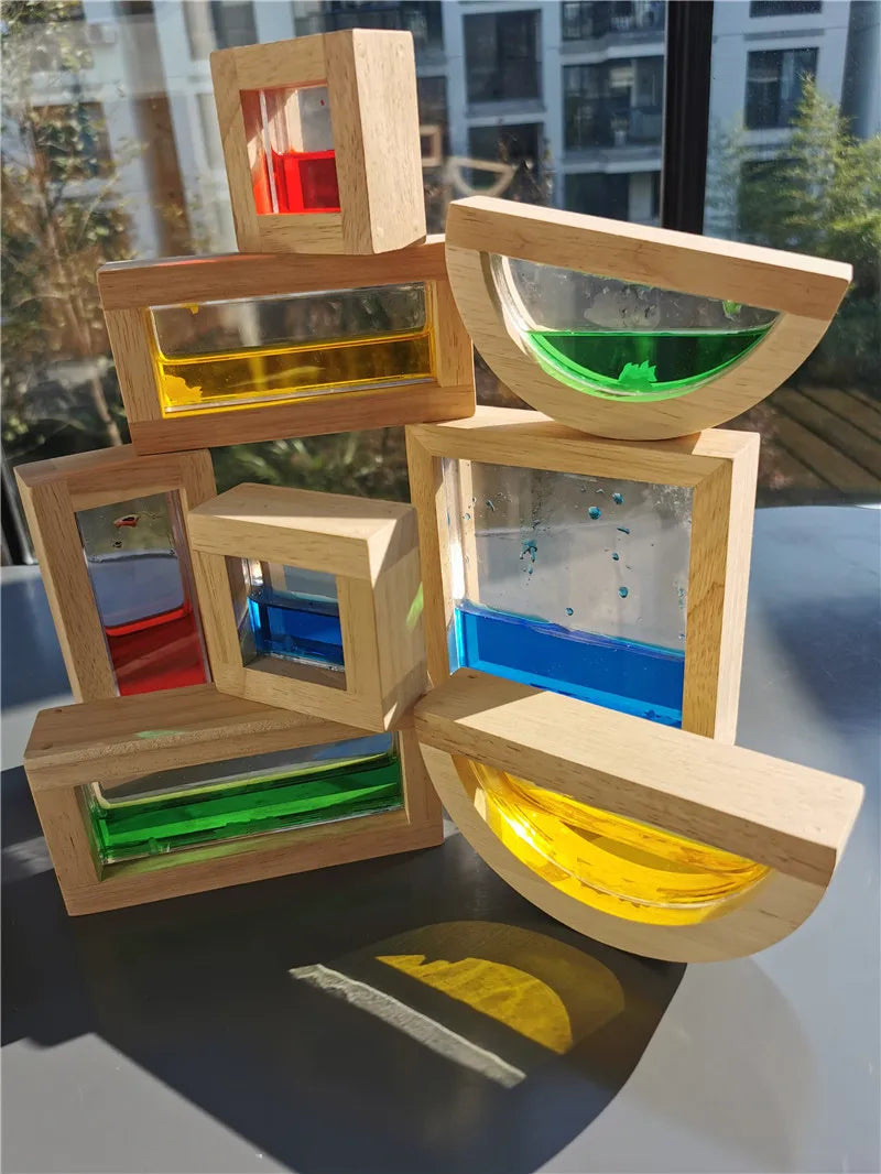 Wooden geometric shapes with colored liquids inside on a reflective surface.