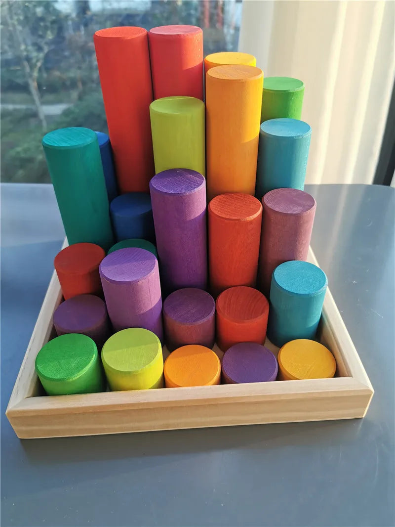 Colorful wooden cylindrical blocks in a wooden tray on a reflective surface.
