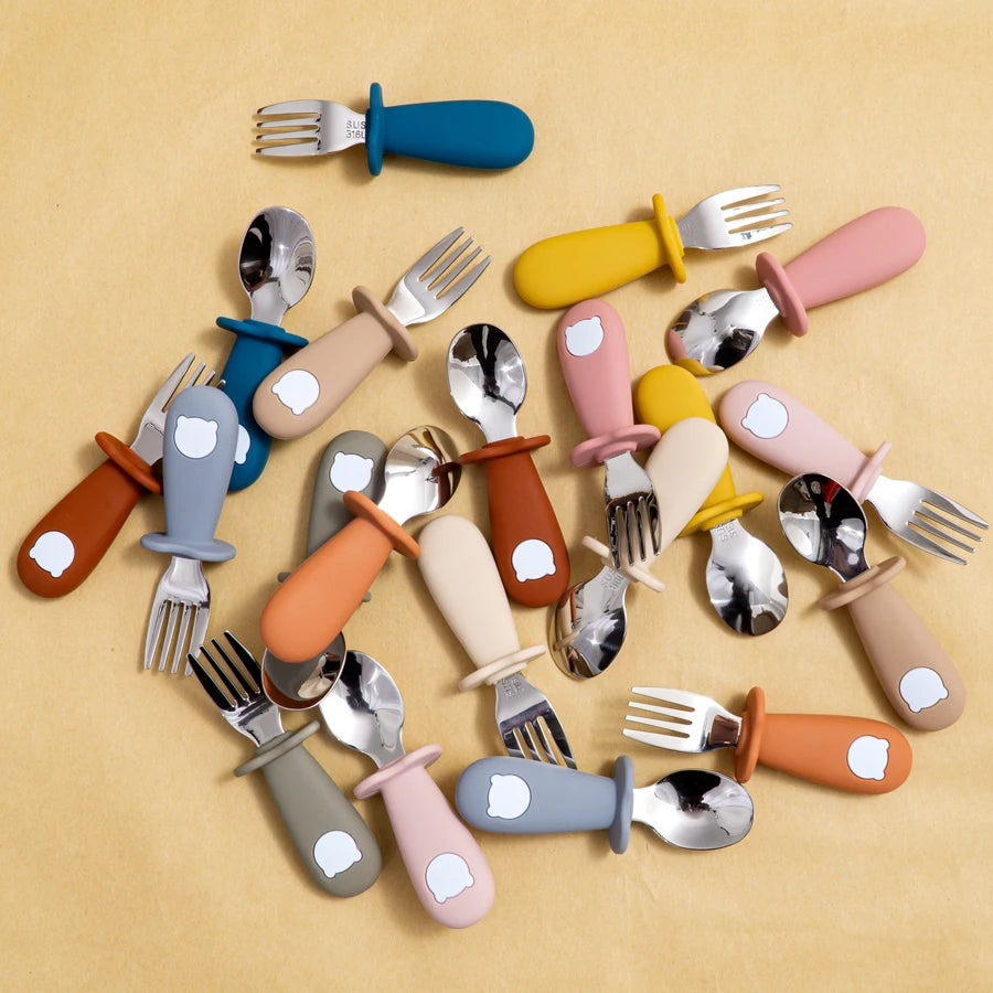 Colorful baby utensils with handles on a beige background