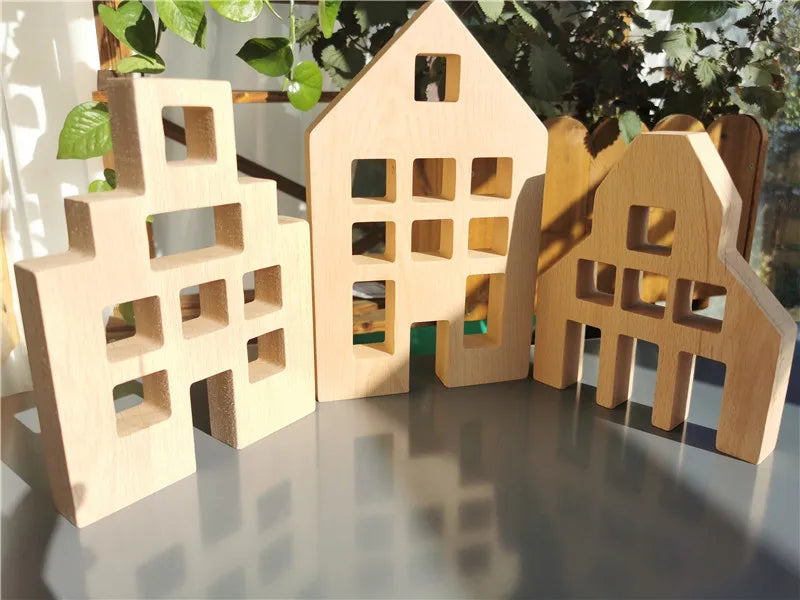 Wooden house models on a reflective surface with greenery in the background