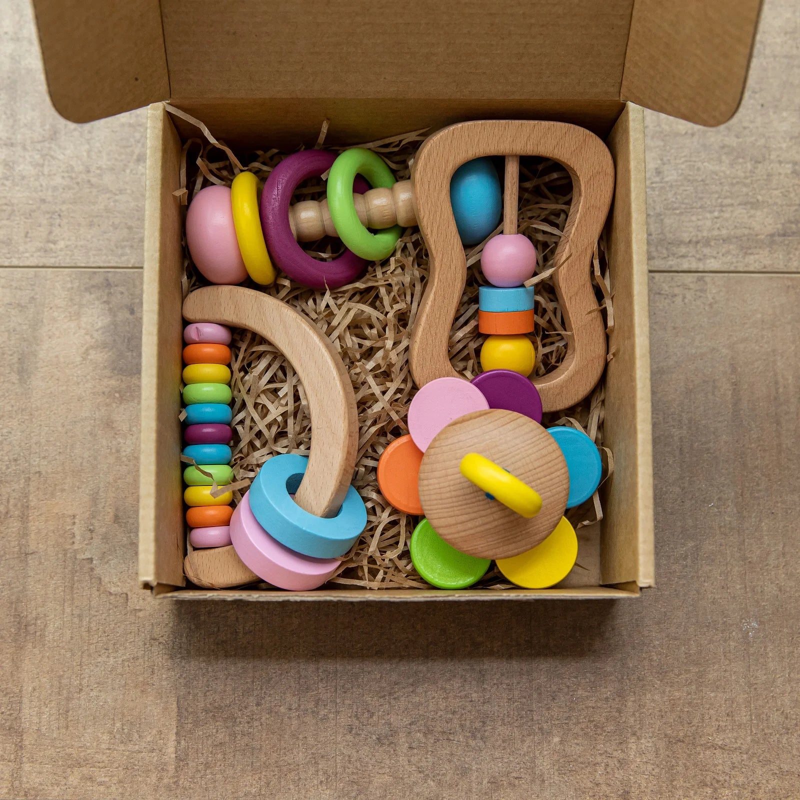 Colorful wooden baby rattles in a cardboard box on a wooden surface