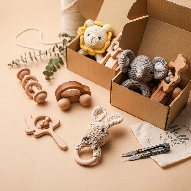 Collection of baby toys including wooden rattle, teether, and soft plush toy on a beige surface with a cardboard box.
