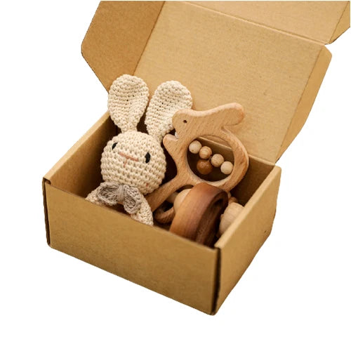 Wooden and crocheted baby toys in an open cardboard box on a white background