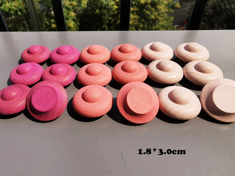 Set of pink and beige round objects on a reflective surface with blurred greenery in the background.