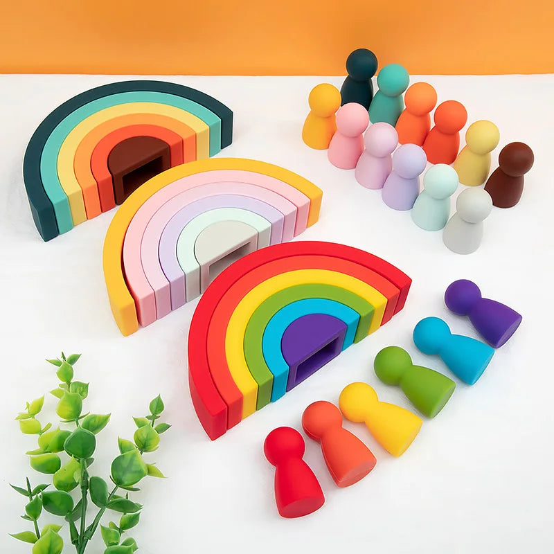Colorful wooden rainbow building blocks and toy figures on a white surface with a green plant.
