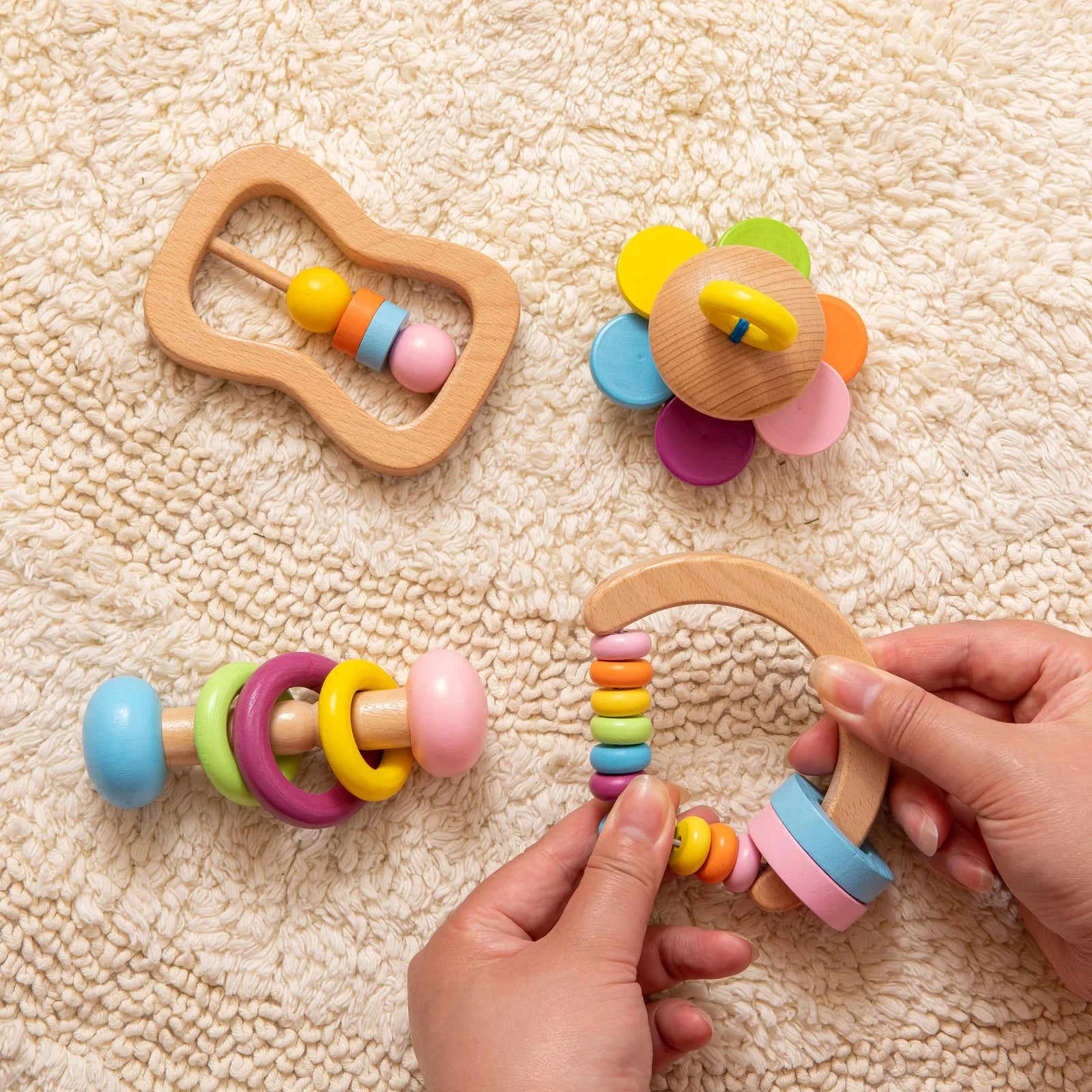 Colorful wooden baby toys on a textured beige surface with hands interacting with one of them.