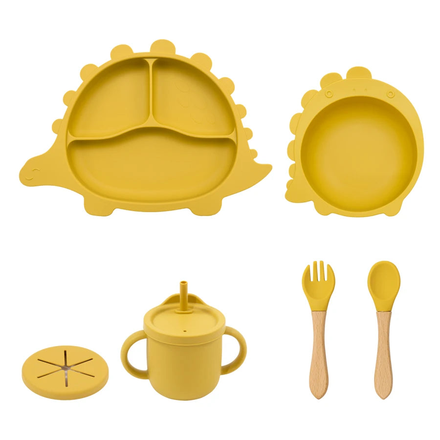 Yellow silicone children's tableware set including plate, bowl, cup, fork, and spoon on a white background.