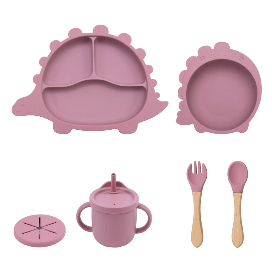 Pink children's dining set including plate, bowl, cup, fork, and spoon on a white background