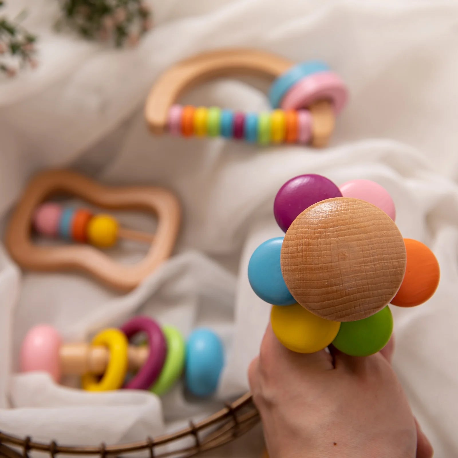 Colorful wooden baby rattle held by a hand with more teething toys in the background.