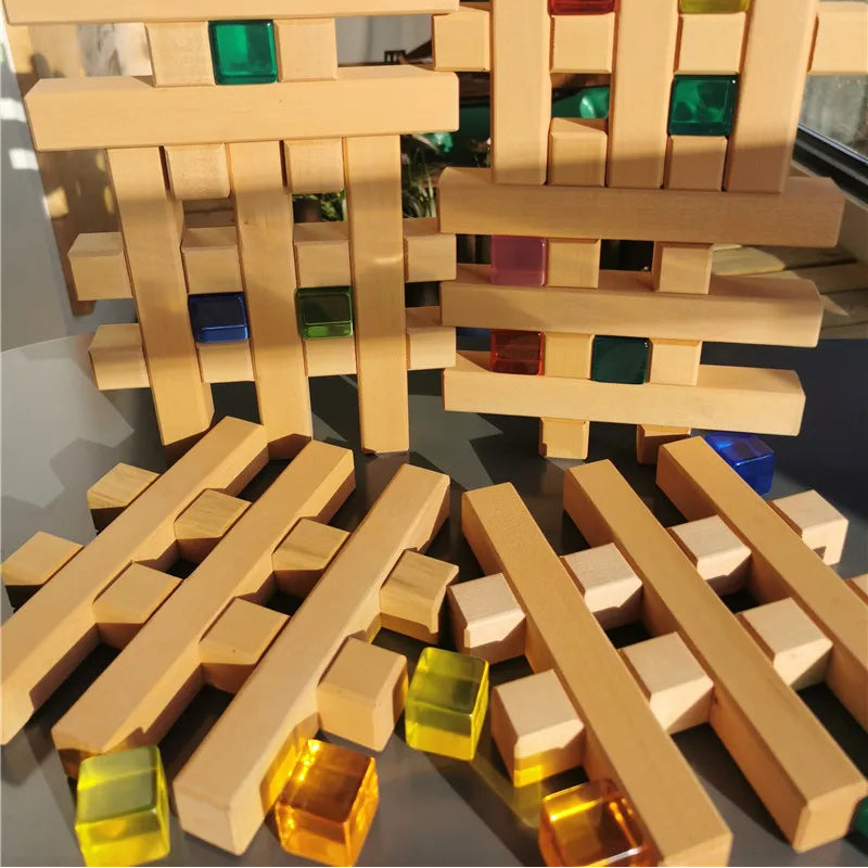 Natural wood block stacking toy with translucent colored square inserts, shown with several loose blocks in the foreground and stacked structures in the background.