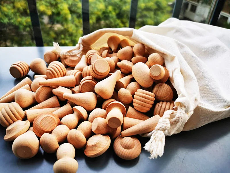 Wooden toys spilling out of a white drawstring bag on a reflective surface with greenery in the background.