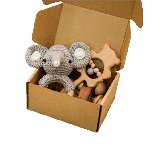 Crocheted mouse toy and wooden rattle in a cardboard box on a white background
