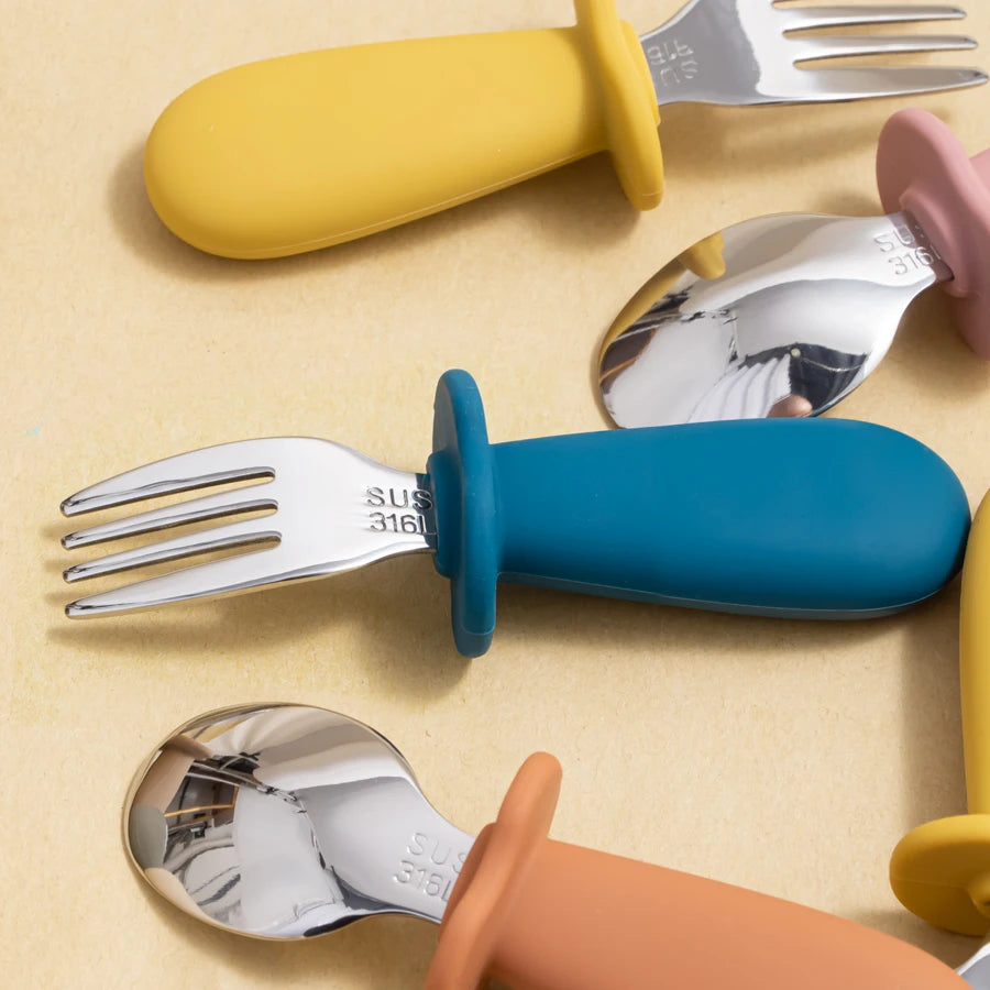 Colorful children's utensils with silicone handles on a beige background