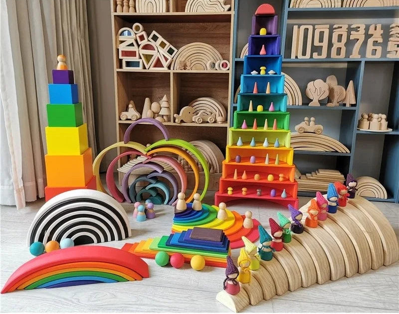 Assorted wooden toys including colorful stacking blocks and rainbow rings on a wooden floor.