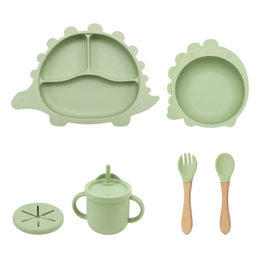 Children's dining set with green silicone plate, bowl, cup, and utensils on a white background