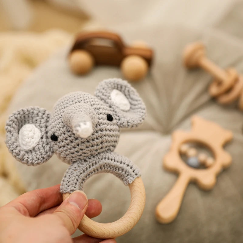 Hand holding a gray elephant-shaped teething ring with wooden teethers in the background.