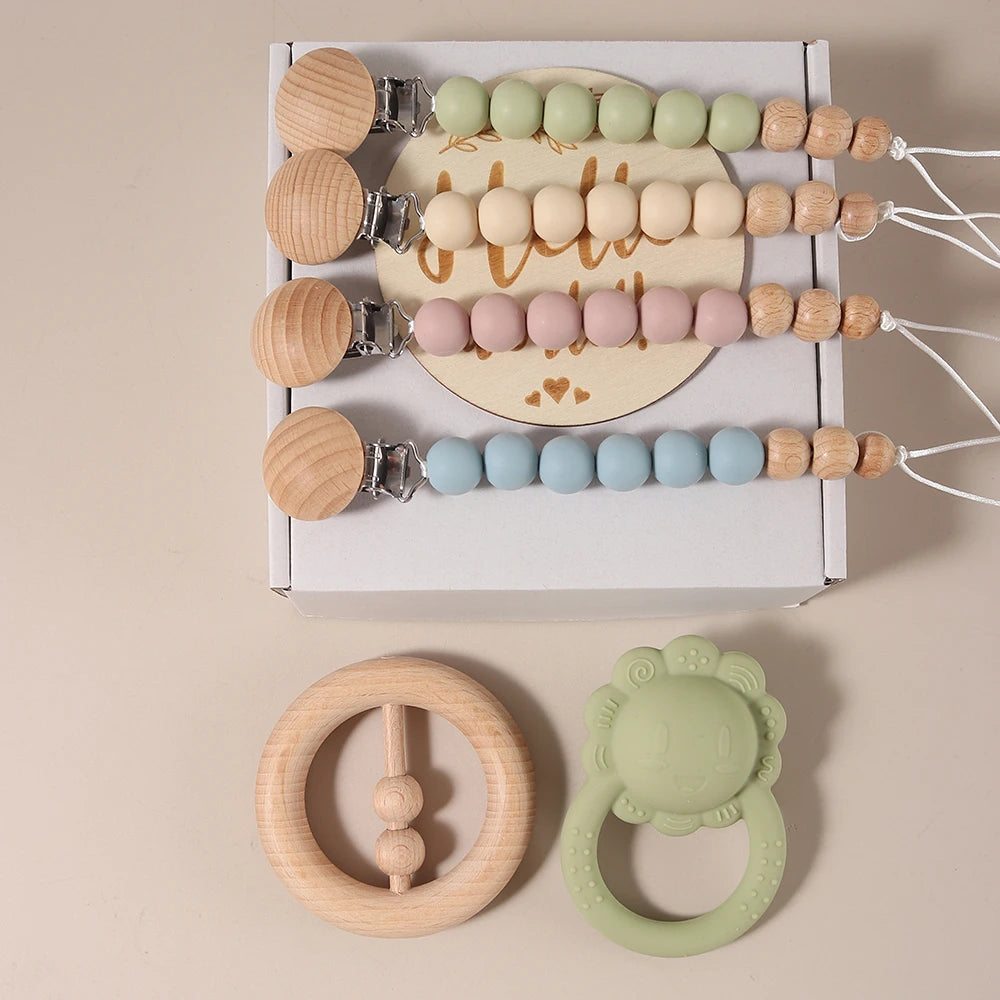 Set of baby teething toys including wooden and silicone rings with a white box on a beige background