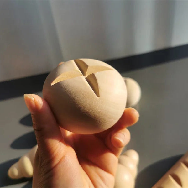 Hand holding a wooden ball with star-shaped cutouts against a neutral background