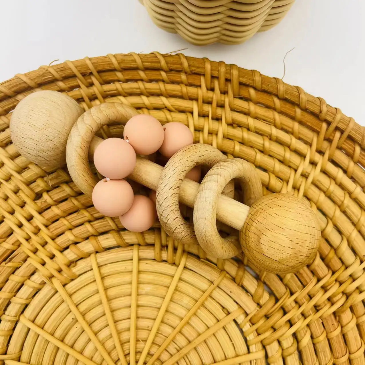 Wooden baby teething ring with pink beads on a woven basket