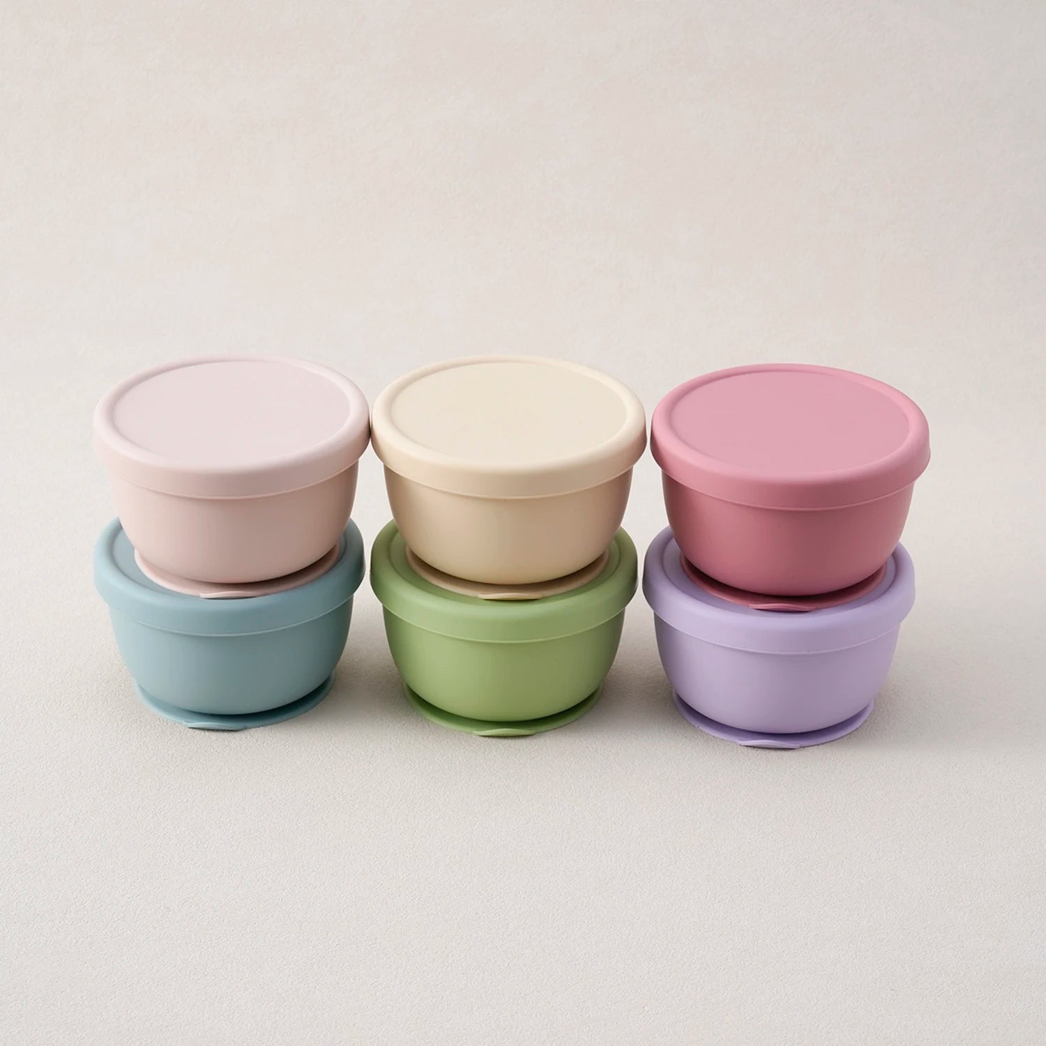 Six silicone suction bowls with lids stacked in pastel colors