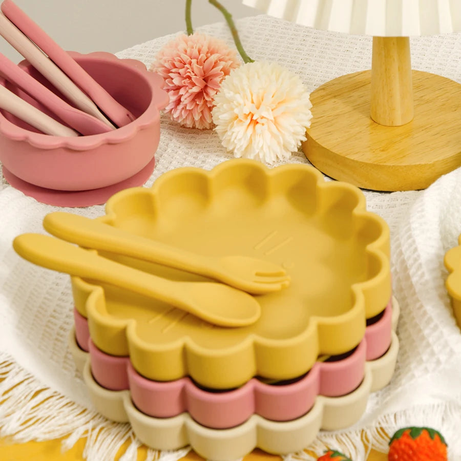 Yellow and pink ceramic cutlery set on a decorative plate with flowers and a candle in the background.