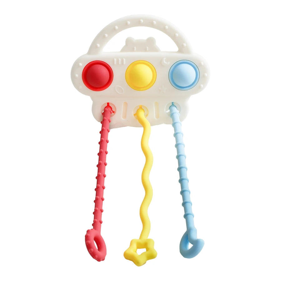 A baby sensory toy with a white plastic handle and three colorful dangling elements: a red textured loop, a yellow wavy tube with a star-shaped end, and a light blue textured loop.