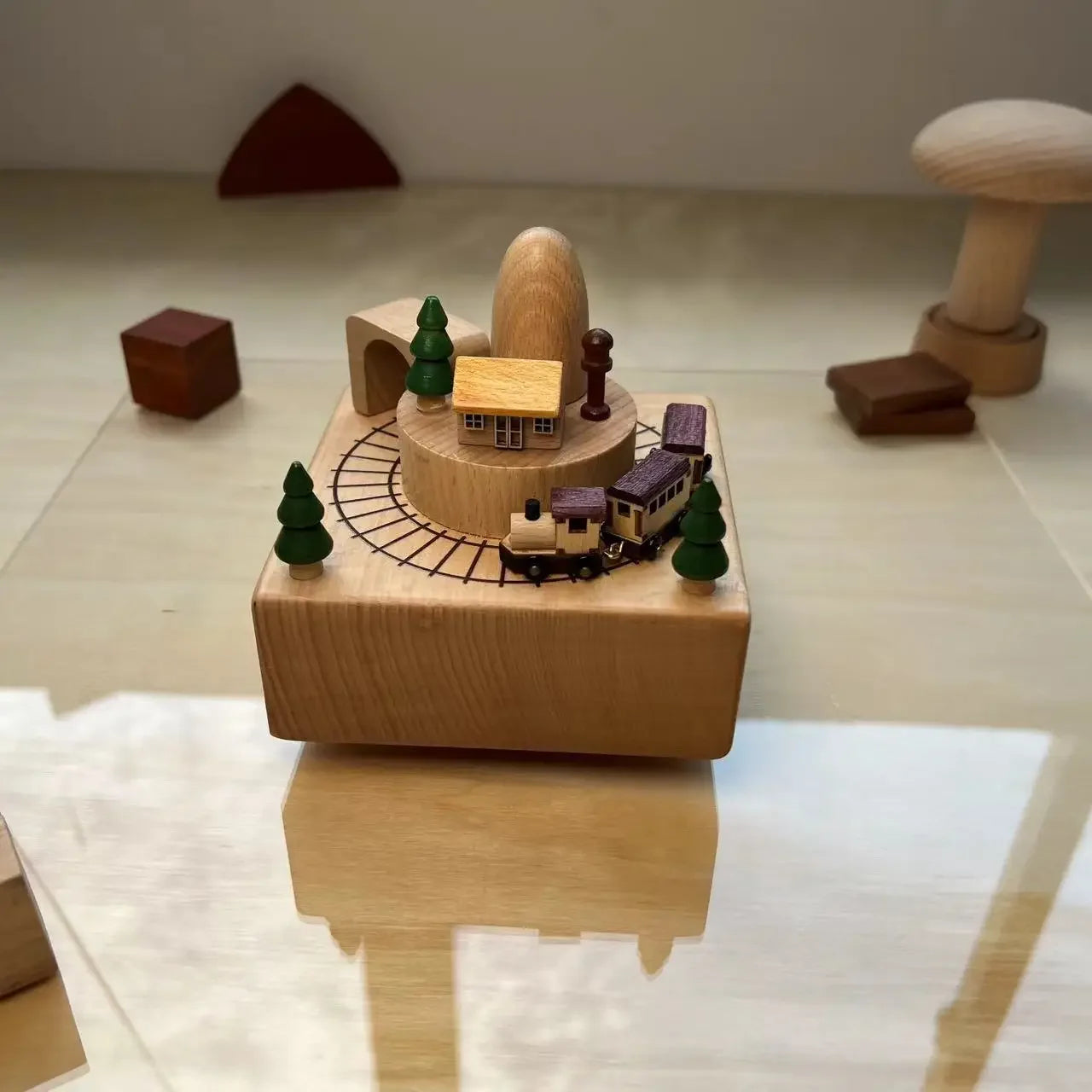 Wooden toy train set with trees and a house on a reflective surface