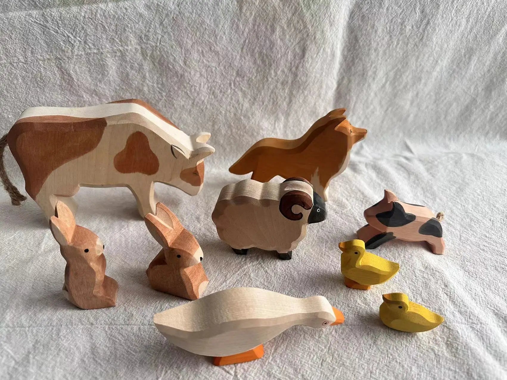 Set of wooden farm animal toys on a white fabric background