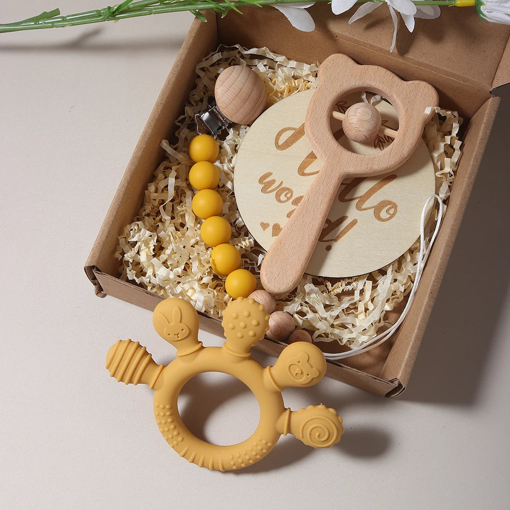Baby teething toys and a wooden rattle in a gift box with flowers in the background.