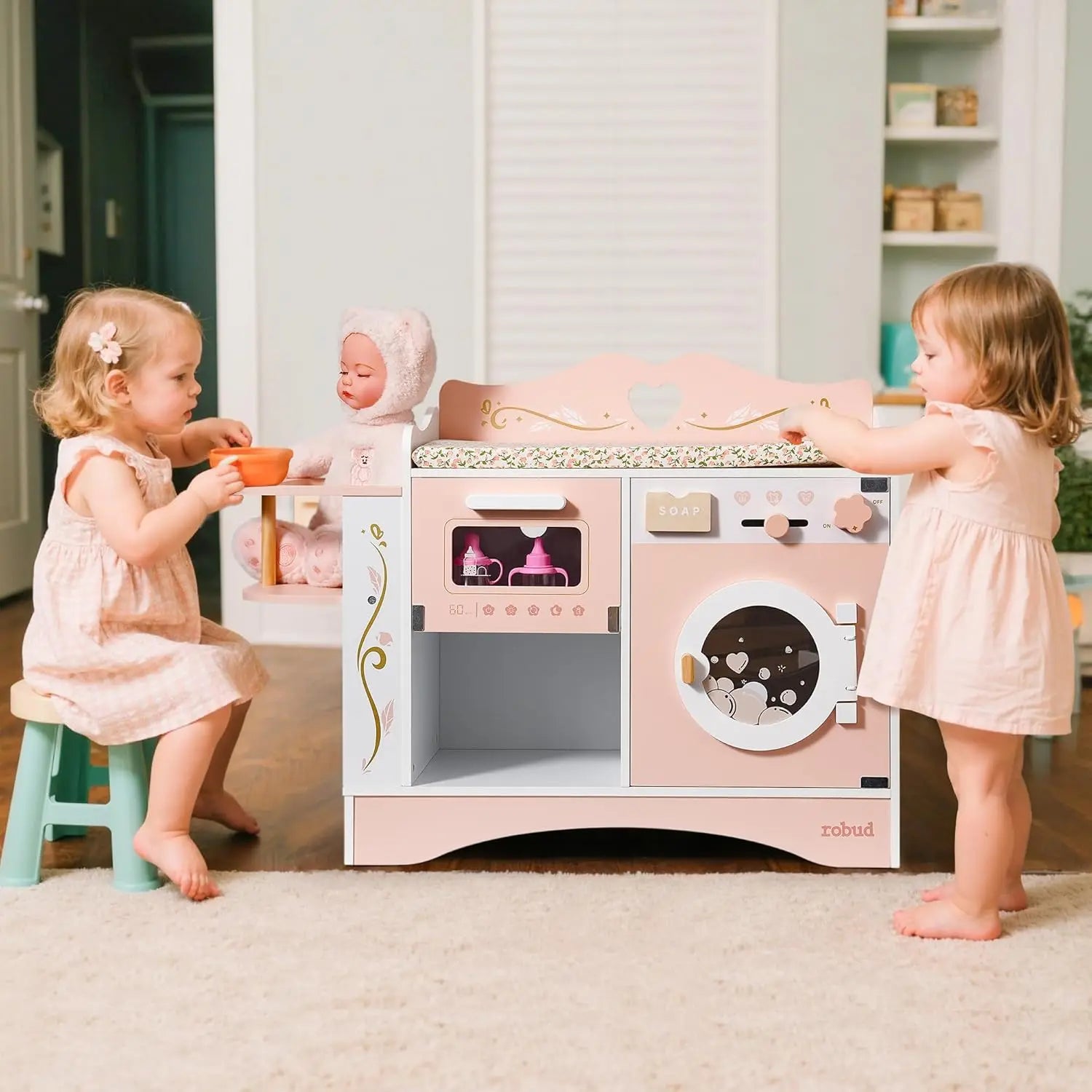 Two young girls playing with a toy kitchen set in a room.