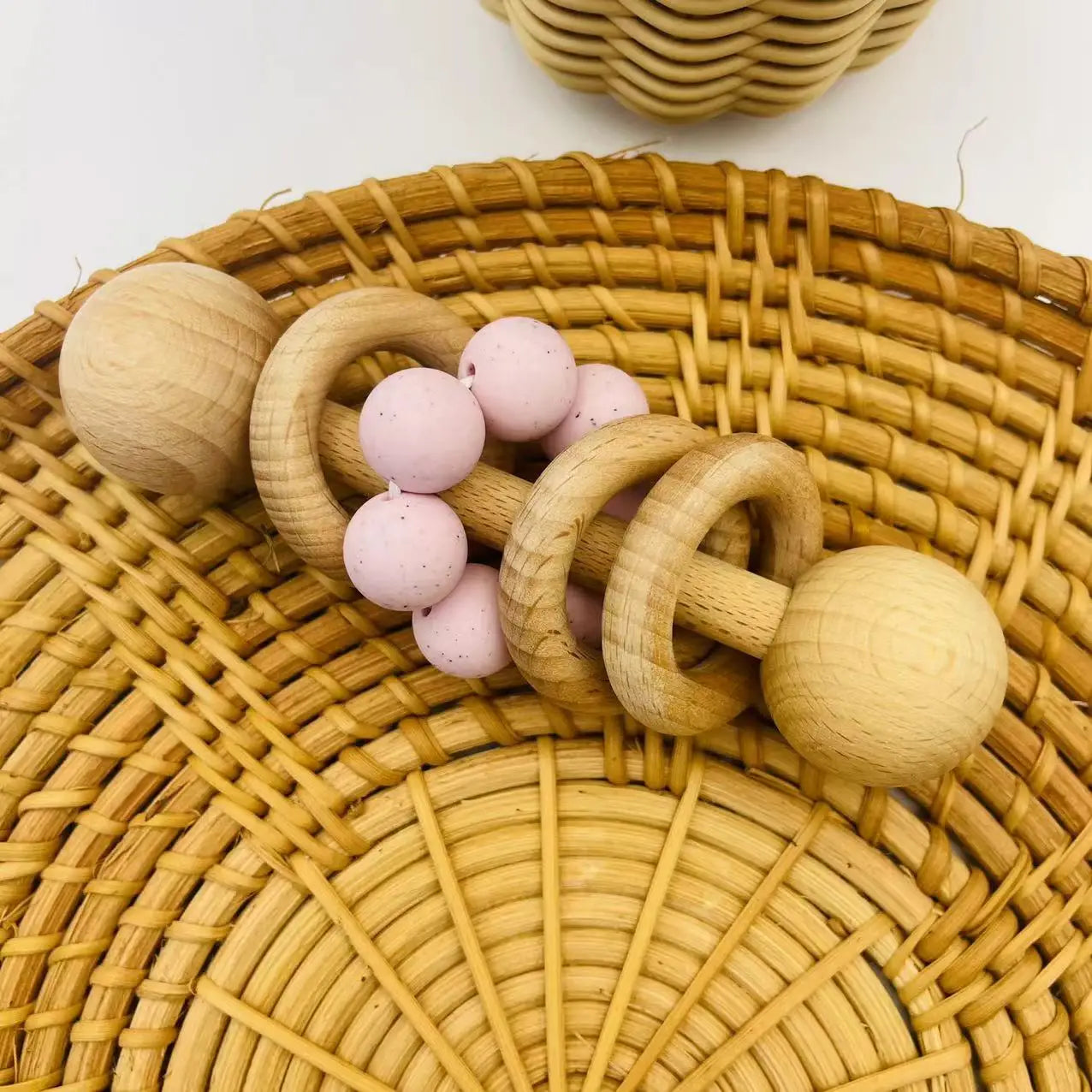 Wooden teething ring with pink beads on a woven surface