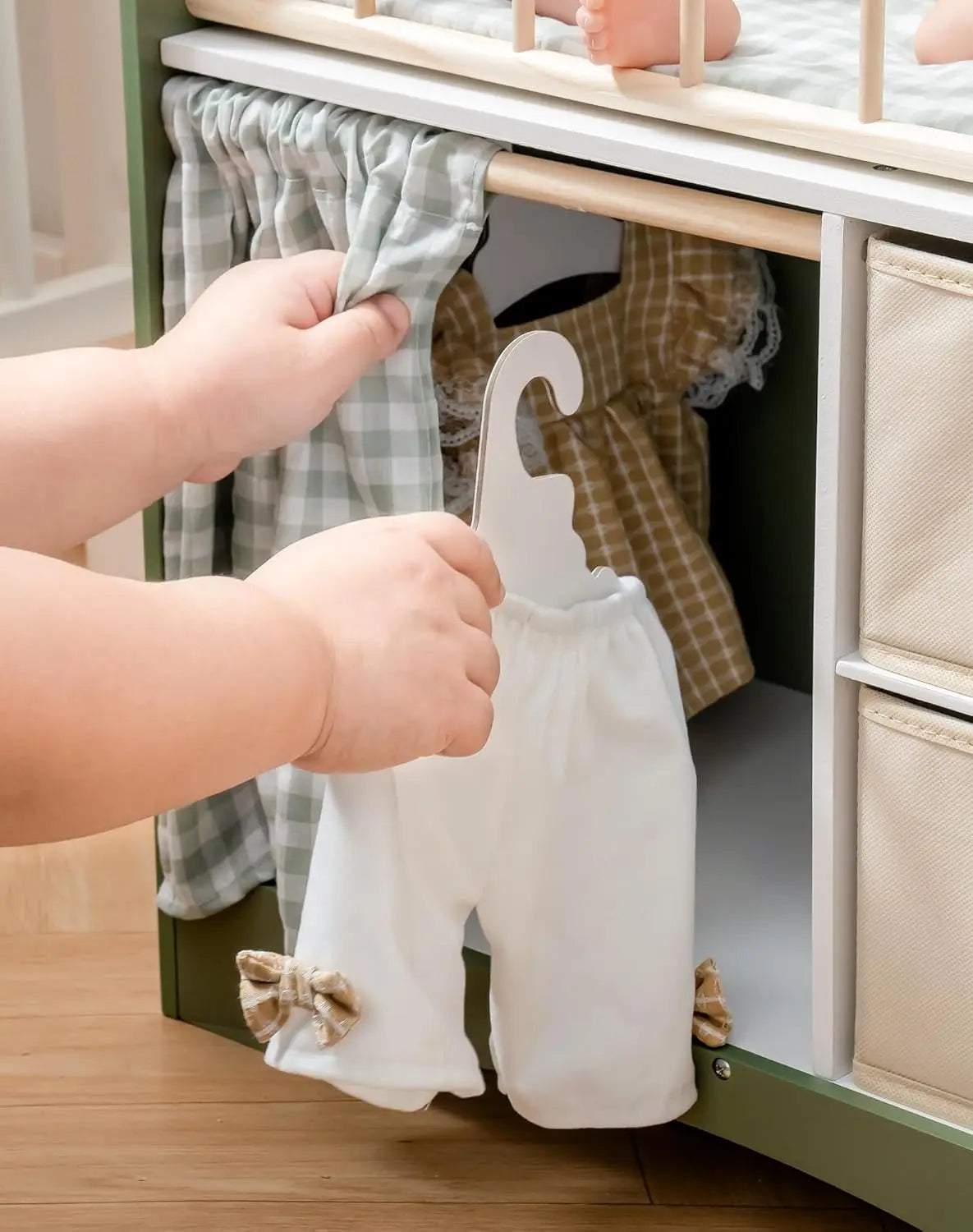 Child's hand holding a white baby outfit with brown accents in front of a cabinet with clothes inside.