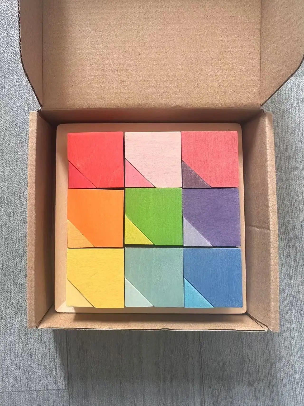 Colorful geometric puzzle blocks in a cardboard box on a gray surface