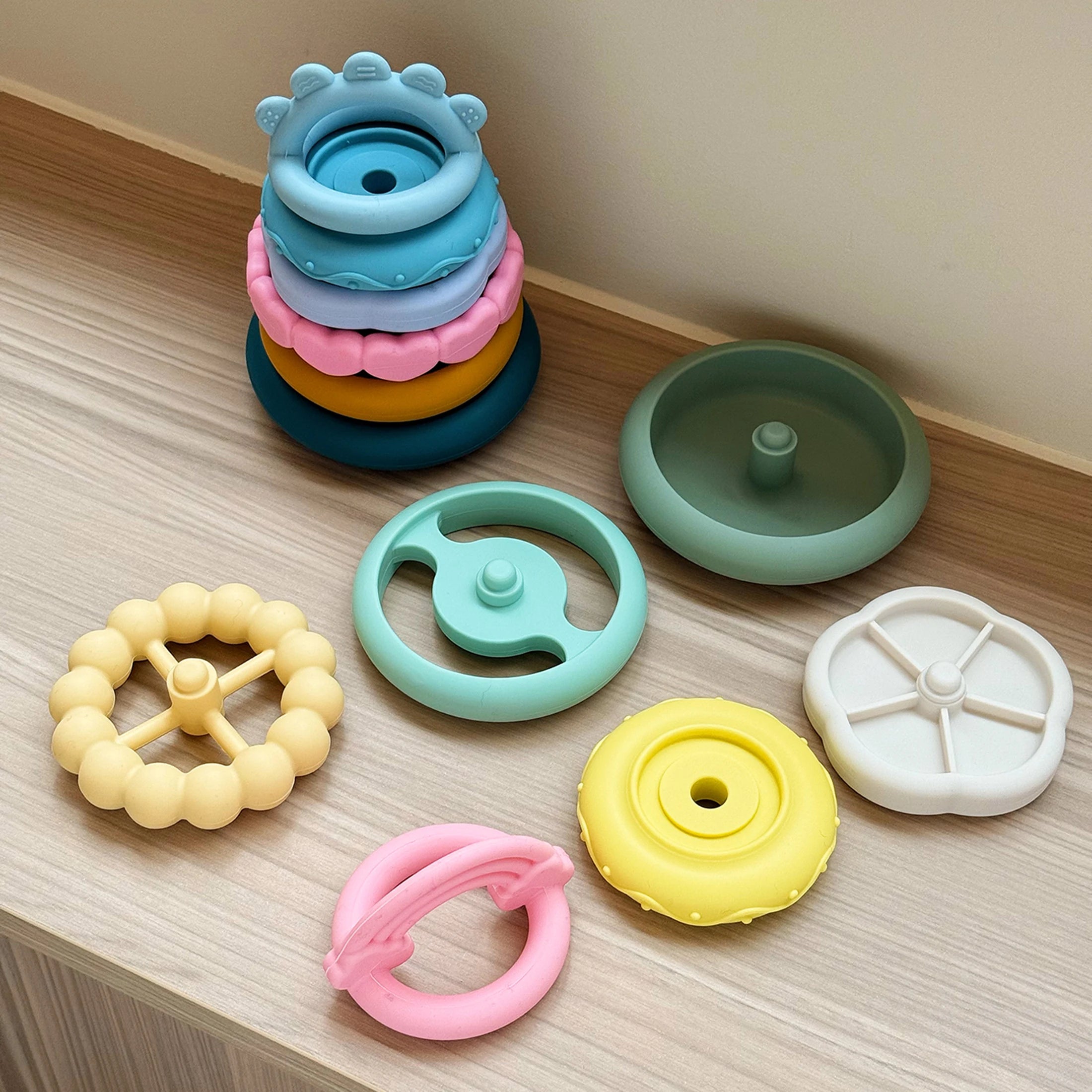 Colorful baby toys including a stacker, teether, and rings on a wooden surface.