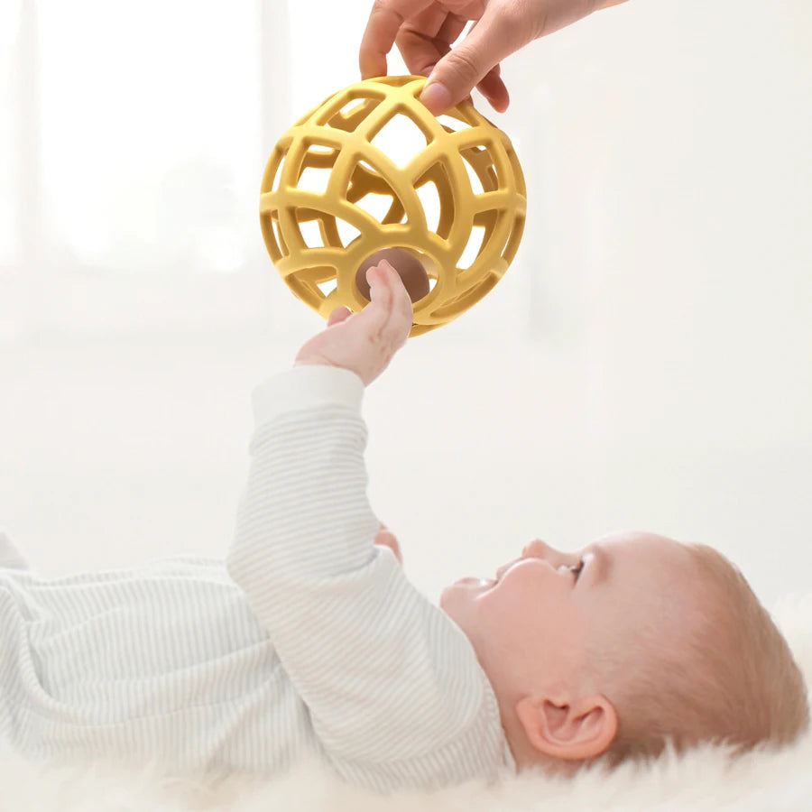Baby reaching for a mustard lattice teether ball