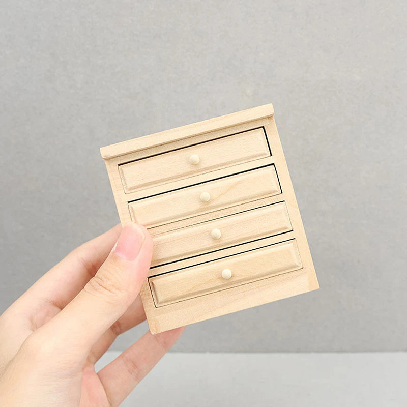 Hand holding a small wooden model of a dresser with drawers against a gray background