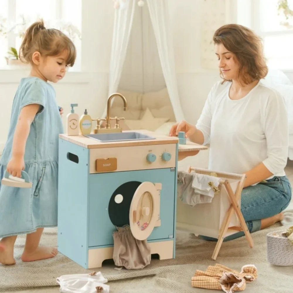 Woman and child playing with a toy washing machine and sink set in a bright room.