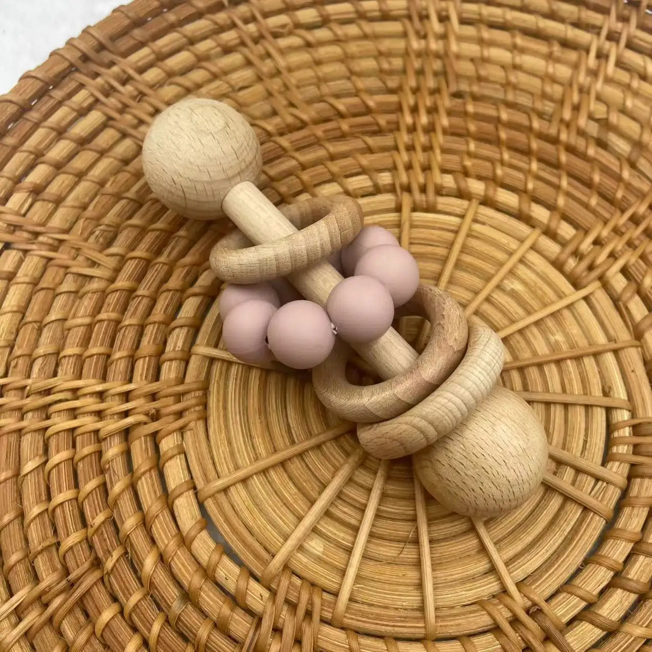 Wooden baby teething ring with pink beads on a woven surface