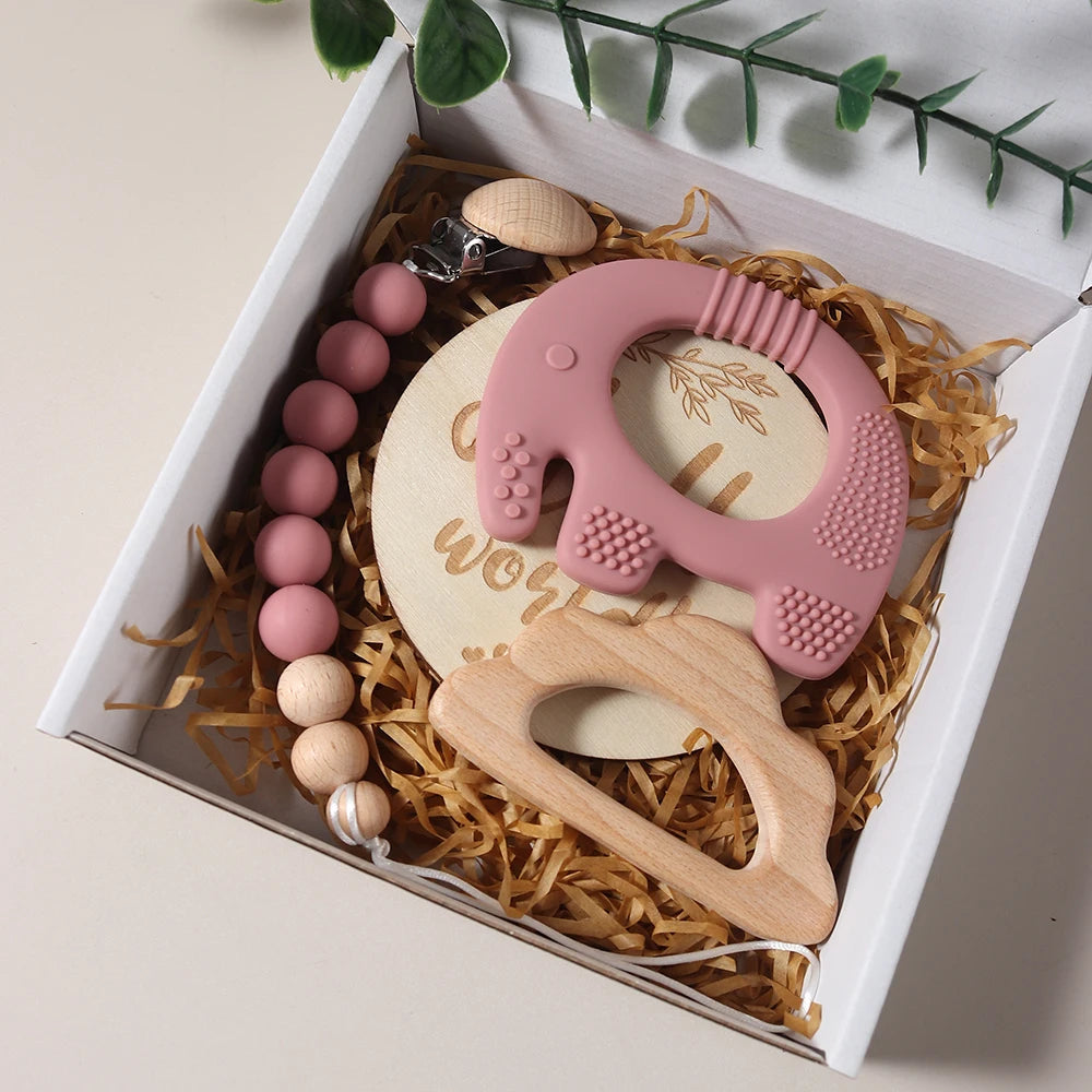 Set of baby teething toys including a pink silicone teether and wooden rattle in a gift box.