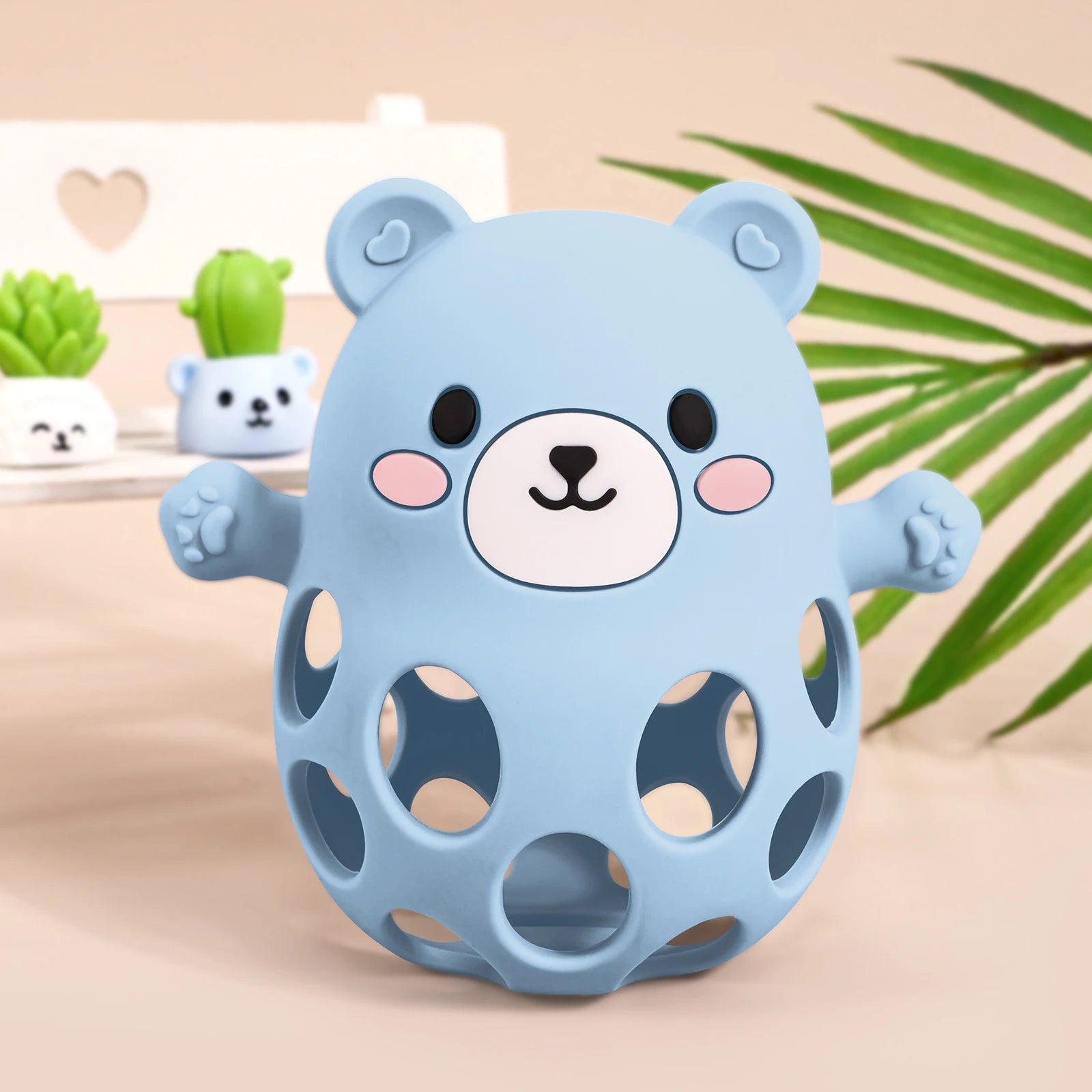 Blue bear-shaped toy with a smiling face on a beige surface with green plants in the background