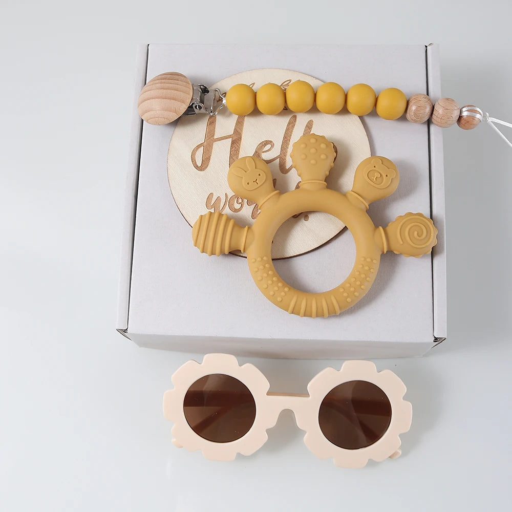 Yellow teething ring with wooden beads and pink sunglasses on a white background