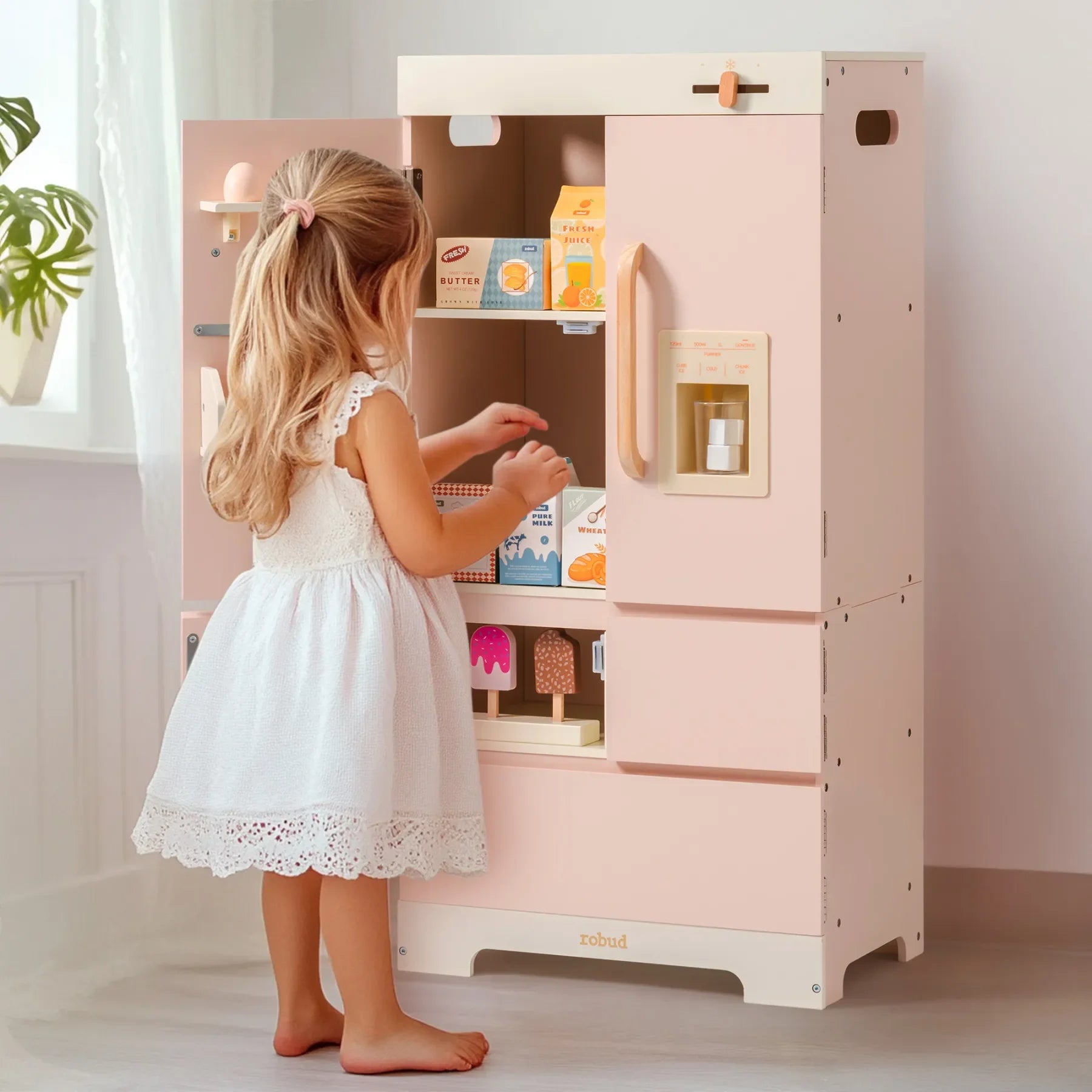 Child in a white dress interacting with a pink toy kitchen set.